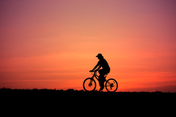 Obraz na płótnie Canvas Silhouette of a man rides a bike at sunset
