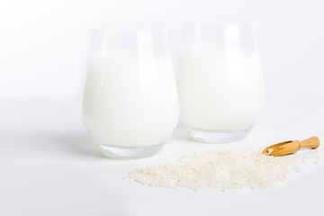 Two glass of vegatarian rice milk and rice grains on white background. Non dairy alternative milk. Concept of proper nutrition and healthy eating. Organic food. Copy space for text, selective focus