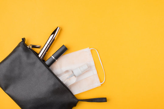 Mask and hand sanitizer as normal part of daily life concept. Top above overhead view flat-lay photo of cosmetic bag packed mask bottle of hand sanitizer in left corner isolated on yellow background