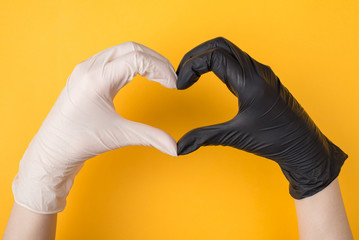 Obraz premium Support during Coronavirus quarantine. Top above overhead view photo of woman's hands in black and white gloves making heart isolated on yellow background