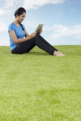Young woman sitting on grass, reading from digital tablet