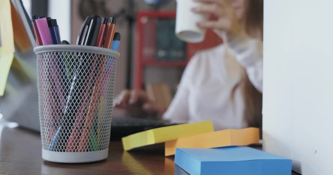 Girl sitting at table, freelancer working at home, abstract plan, out of focus, girl typing, drinking coffee, desk mess, stickers, pens and pencils, creative environment, writer at work, designer