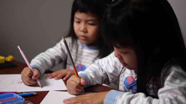 Twin Thai girl learning and drawing on white paper in slow motion. Child happy and paint color on table in 4K resolution