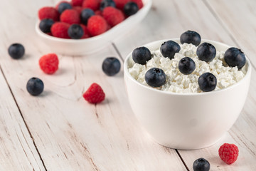 Cottage cheese or curd with raspberries and blueberries in white ceramic bowls on a wooden background