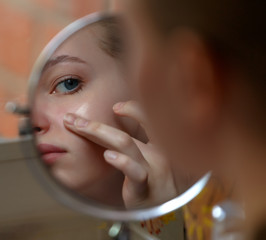 Girl teenager checking pimples on her face in front of round mirror