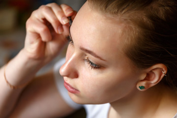 Fototapeta premium Portrait of a girl applying mascara on her eye lashes view from above