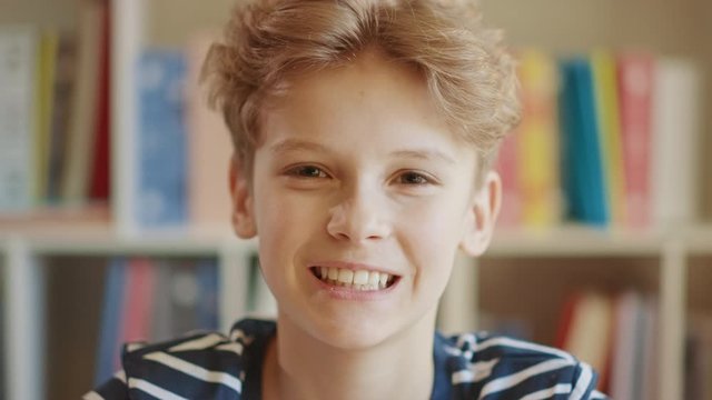 Close-up Portrait of a Happy Smart Young Boy, Smiling and Looking at Camera. Background Blurred Bookshelf.