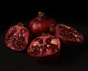 close up of a fruit still life, pomegranates cut open on a black studio background.