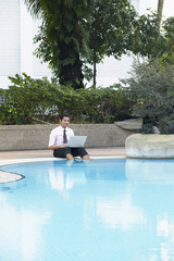 Young businessman using laptop by the swimming pool