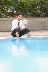 Young businessman using digital tablet by the swimming pool