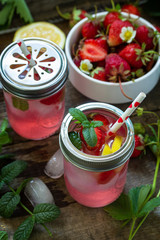 Refreshing Summer drink. Lemonade with fresh strawberries, ice and lemons on a rustic wooden table.