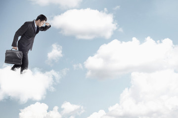 Fototapeta na wymiar Young businessman standing on clouds, looking below