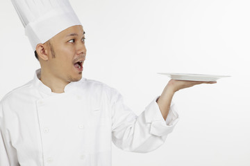 Asian chef holding a plate, looking surprised