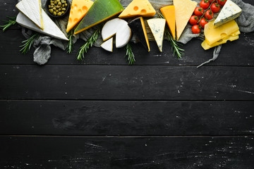 Variety of cheese and cheese slicing on black wooden background. Top view. Free space for your text.
