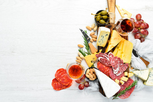 Italian antipasti wine snacks set. Cheese variety, salami and grapes on a white wooden background. Italian cuisine. Top view. Free space for your text.