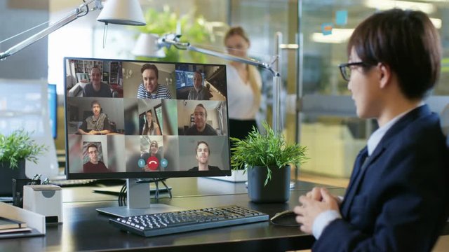 In the Office: Businessman Uses PC Conference Video Call Software App to Talk with Group Remote Working Colleagues and Coworkers. Businesspeople doing Online Meeting, Working from Office, Home Office