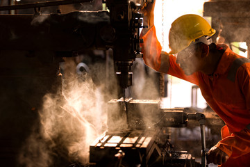 Male workers wear safety glasses, control lathes to drill components. Lathe factory operations in Asia