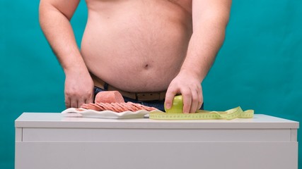 man with a fat belly chooses between sausage and a green apple. The concept of diet and willpower.