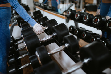 Close up of hands of girl with gloves while lifting weights in the gym. COVID - 19 virus protection