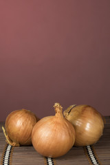 Three onions on board cutting, red background