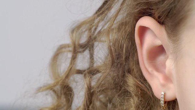 Closeup female ear with earrings front view. Right ear of curly young woman on gray background. Human hearing organs. Human body part. Head anatomy