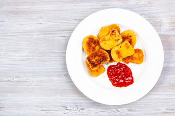 top view of fried chicken nuggets with ketchup on white plate on gray wooden board