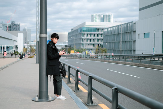 Young asian man waiting for bus and taxi on sidewalk