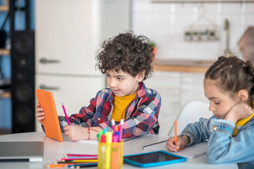Boy and girl sitting at round table, holding tablets, busy with their assignments