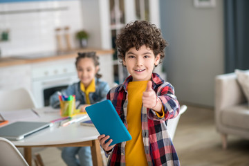 Curly boy standing with tablet, smiling into the camera