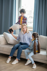 Curly boy and dark-haired girl fighting, boy holding cushion, blonde female trying to calm them down
