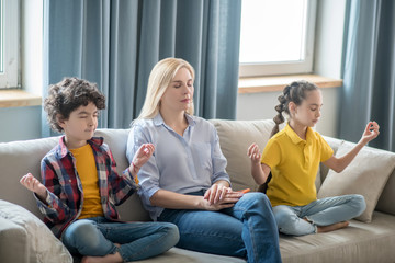 Obraz premium Curly boy, dark-haired girl and blonde female sitting on sofa, meditating