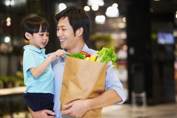 Father holding a bag of groceries and carrying son