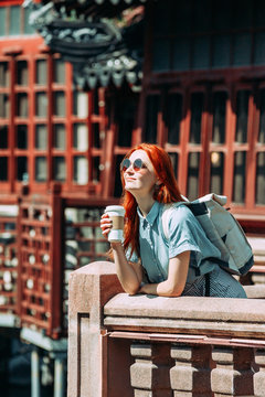 Red hair femaletTourist wearing blue shirt and sunglasses drinking take away coffee and enjoying the view of Yuyuan Garden in Shanghai, china. Asia tourism travel. Travel lifestyle concept
