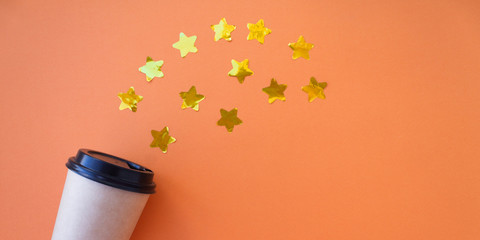 Banner Coffee to go concept. Disposable craft cup with black plastic cover on a trendy orange background with gold stars confetti. Place for text. Flat lay style. Top view