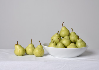 close up portrait of group of green pears on white table cloth against a studio background.