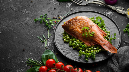 Baked sea red perch with green peas on a black stone plate. Top view. Free copy space.