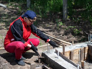 Senior Caucasian woman removes formwork from a strip foundation