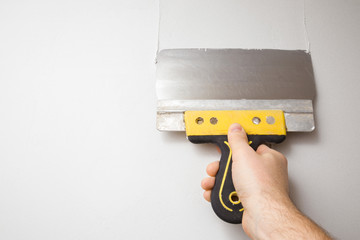 Worker hand using spatula and plastering wall with white putty. Closeup. Point of view shot.
