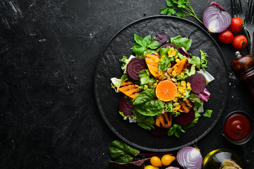 Salad: beetroot, pumpkin, corn and lettuce in a black plate on a black background. Top view. Free space for your text.
