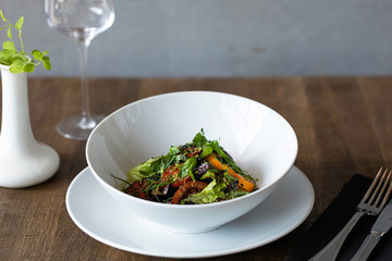 salad with meat and herbs in a white plate on a wooden background
