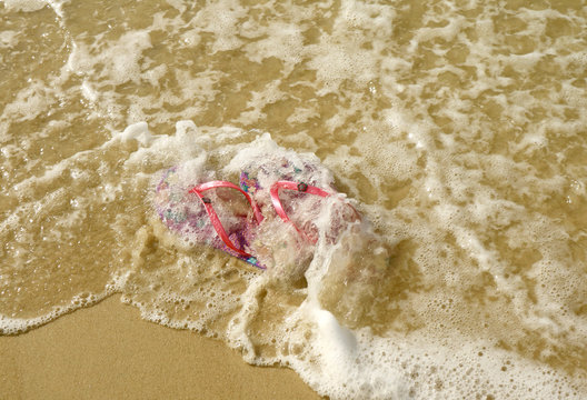 Pair of vibrant pink flip-flops sandals on the beach crashing by sea waves