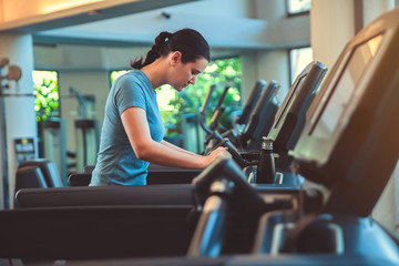 Fototapeta na wymiar Attractive young sports woman is working out in gym doing cardio training running on treadmill in sport club