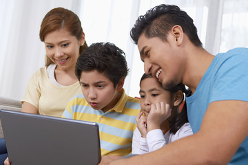 Family of four sitting and using laptop together