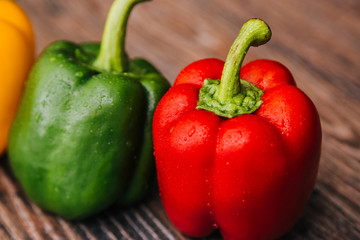 Sweet pepper multicolored on a dark wooden background. Red, yellow and green peppers are on the table. Bright vegetable