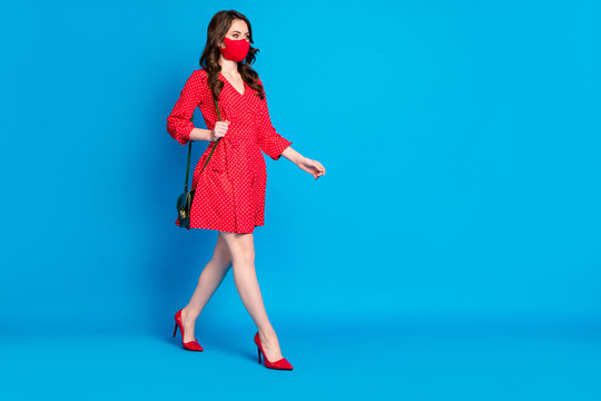Full length profile photo of pretty lady keep social distance walk breathe fresh air alone street wear dotted red dress stilettos clutch protect facial mask isolated blue color background
