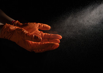 Obraz na płótnie Canvas spraying a disinfection spray on orange latex gloves on a black background
