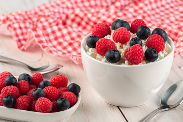 White ceramic bowls with cottage cheese and fresh berries on wooden table with napkin . Diet breakfast