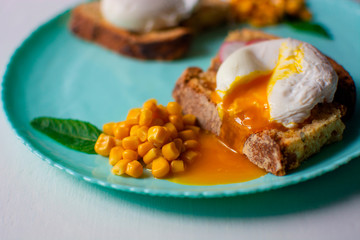 yolk pours from an egg onto a piece of bread and a turquoise plate. 
poached eggs with bread and corn