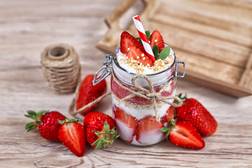 Healthy strawberry fruit dessert with yogurt,  chia seeds and puffed quinoa grains layered in jar surrounded by berries on wooden background