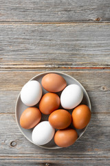 Eggs in a plate on the kitchen table. White and brown eggs for cooking. Chicken eggs on a wooden culinary background. Concept of preparation for baking. Top view with space for text